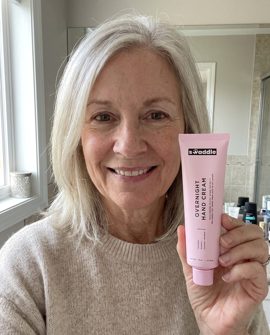 A woman in her sixties holding the Swaddle Overnight Hand Cream in her bathroom